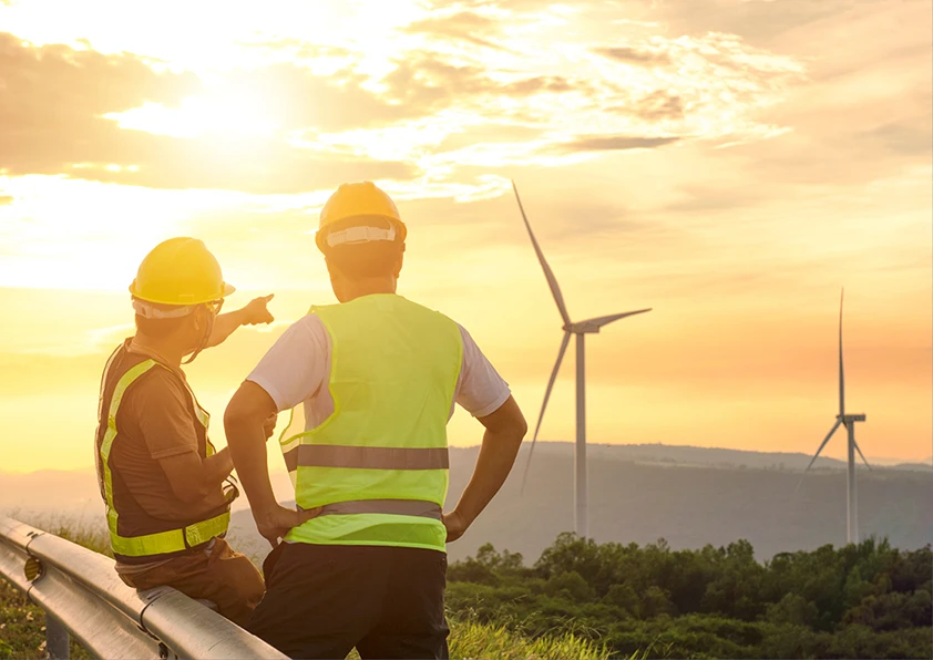 Two men working on a wind turbine facility at sunset